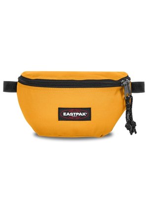 Sac banane Eastpak jaune porté sur un jean bleu clair avec les mains dans les poches et un haut sombre partiellement visible.