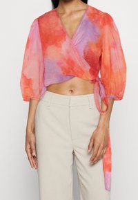 Top corto fluido cruzado en naranja y rosa con un patrón de acuarela, que presenta mangas abullonadas y un detalle de lazo en el lado.