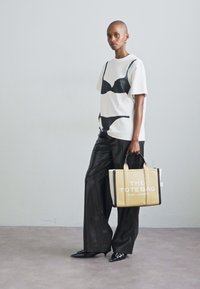 White t-shirt with black bra graphic, black wide-leg trousers, and beige tote bag with white lettering. Black pointed shoes, minimal accessories.