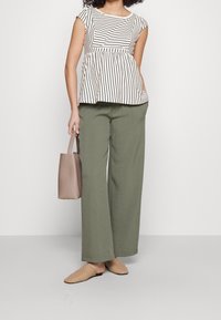Pruhovaný top s krátkým rukávem v krémové a tmavě hnědé barvě; volné kalhoty širokého střihu v olivově zelené; tkané béžové nazouvací boty; malá taupe kabelka.
