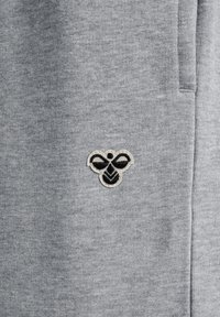 Grauer Sweatstoff mit einem kleinen, gestickten Bienenlogo in Schwarz und Creme auf der linken Seite, strukturiert mit einem Rippenmuster.