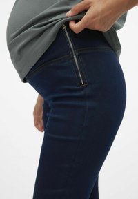 Materinski jeans v temno modrem denim materialu, z bočnim zadrgo in ojačanim šivom. Prilegajo se okoli pasu.