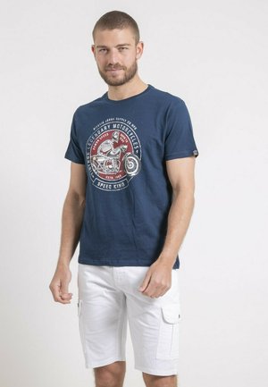 T-shirt en coton bleu marine avec une impression graphique d'une moto et d'un crâne sur le devant, associé à un short cargo blanc.