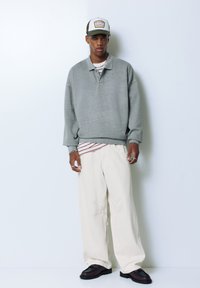 Lys grå oversized sweater med krave, parret med løse cremefarvede bukser og mørke sko. Har en stribet skjorte under.