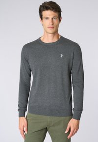 Maglione lavorato a maglia grigio scuro con scollatura rotonda e polsini a costine, caratterizzato da un piccolo emblema sulla zona sinistra del petto.