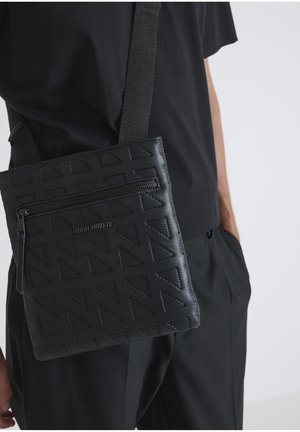Borsa a tracolla nera con motivo triangolare testurizzato, tasca frontale con zip e tracolla intrecciata. Presenta un dettaglio con il marchio sulla parte anteriore.