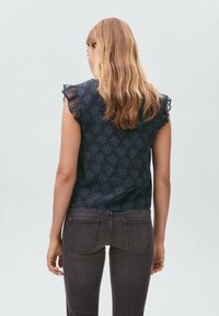 Top senza maniche floreale navy con dettagli arricciati sulle spalle, abbinato a pantaloni grigi scuri con un design aderente e una superficie liscia.