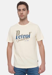 Cremefarvet bomulds t-shirt med "Petrol Industries" grafik i blå og beige. Korte ærmer og rund halsudskæring.