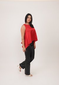 Top in raso rosso con orlo asimmetrico, abbinato a pantaloni in ecopelle nera e sandali con tacco bianchi. Texture liscia e design moderno.