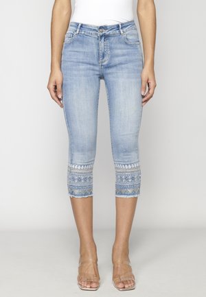 Light blue cropped denim jeans with embroidered geometric patterns and small beads near the hems, worn with clear strap heels.