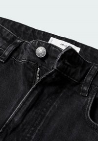 Jean en denim noir avec bouton visible et fermeture éclair partiellement ouverte, montrant l'étiquette de la marque à l'intérieur de la ceinture.