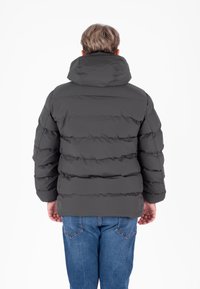 Giubbotto imbottito grigio scuro con cappuccio, caratterizzato da un design trapuntato e tasche laterali, abbinato a jeans di denim blu.