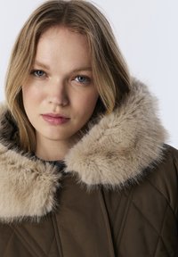 Bruine gewatteerde jas met een brede nep-vacht kraag in lichtbruin. De jas heeft een moderne snit en een gestructureerde stof.