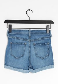 Jeansshorts i ljusblå tvätt, med uppvikt nederkant, två bakfickor och midja i normalhöjd, hängande på en svart plastgalge.