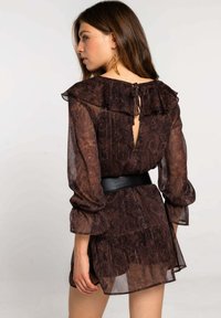 Vestido de gasa marrón con detalles de volantes, escote bajo y un cinturón negro en la cintura; patrón de paisley texturizado en toda la prenda.