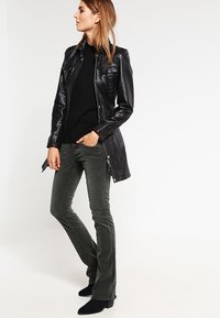 Veste en cuir noir avec des détails zippés et à pression, associée à un haut noir ajusté et un pantalon flare vert olive. Des bottines noires complètent le look.