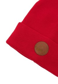 Czerwony dzianinowy beanie z podwijanym mankietem, z okrągłą brązową skórzaną łatą z wytłoczonym wzorem. Miękka tekstura i intensywny kolor.