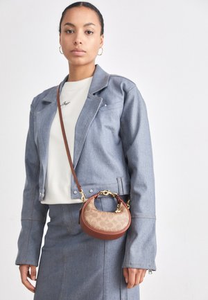 Pequeña bolsa marrón y beige con un patrón de logo clásico, herrajes dorados y forma curvada, combinada con una chaqueta y falda de mezclilla.