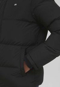 Black puffer jacket featuring a quilted design, elastic cuffs, and side pockets, with a small logo on the chest. Smooth, durable fabric.