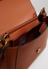 Borsa a mano in ecopelle marrone con finitura testurizzata, dotata di chiusura magnetica, tasca interna con cerniera e dettagli in metallo color oro.