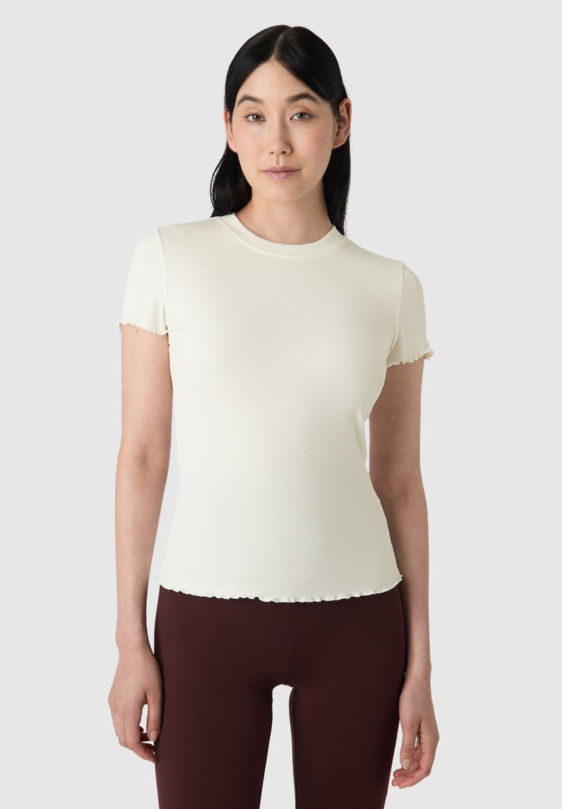 Krátký rukáv, žebrovaný krémový top s kulatým výstřihem a vroubkovaným lemem. Pairs with bordó legínami pro kontrast.