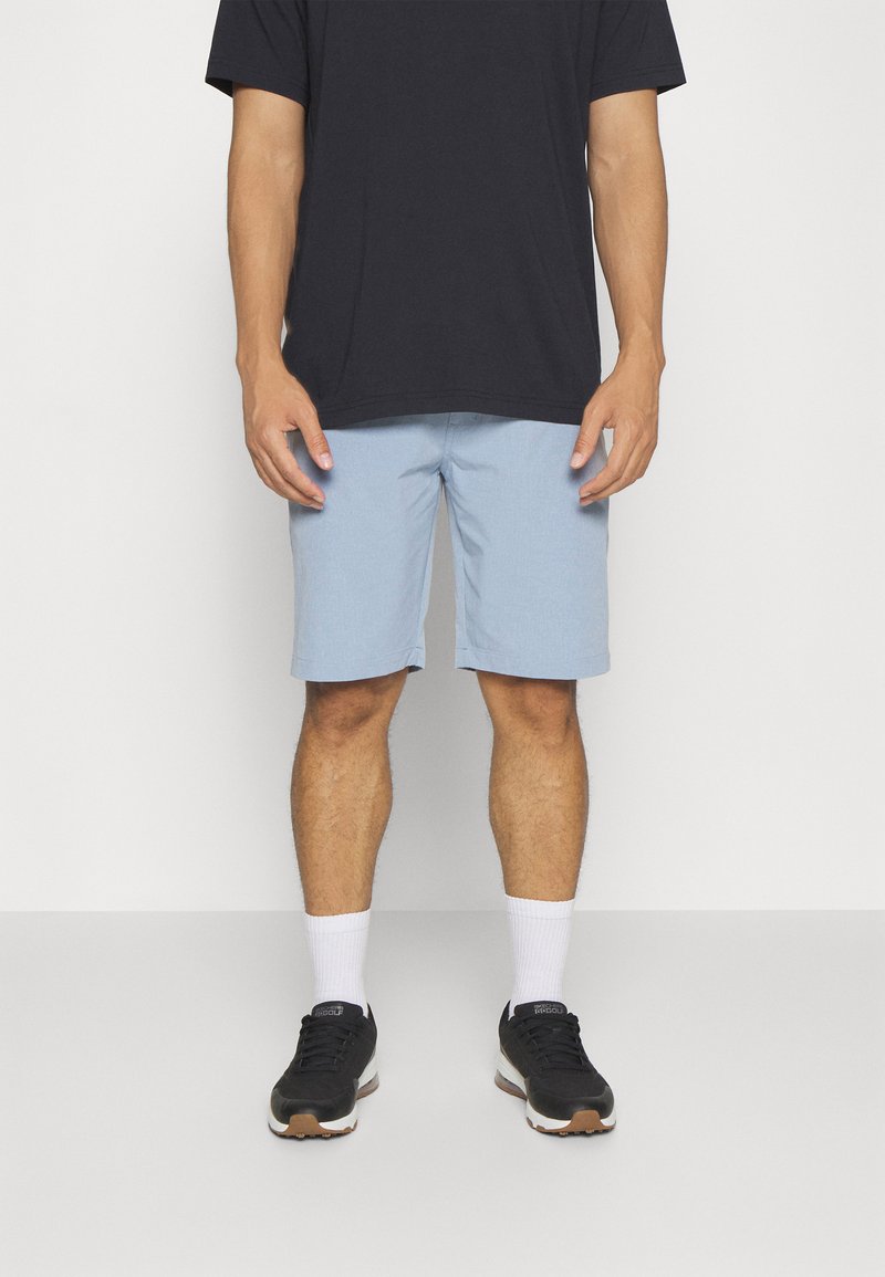 Hellblaue Shorts aus atmungsaktivem Material, mit flachem Frontschnitt, Taschen und geradem Schnitt, kombiniert mit einem schwarzen T-Shirt und Turnschuhen.