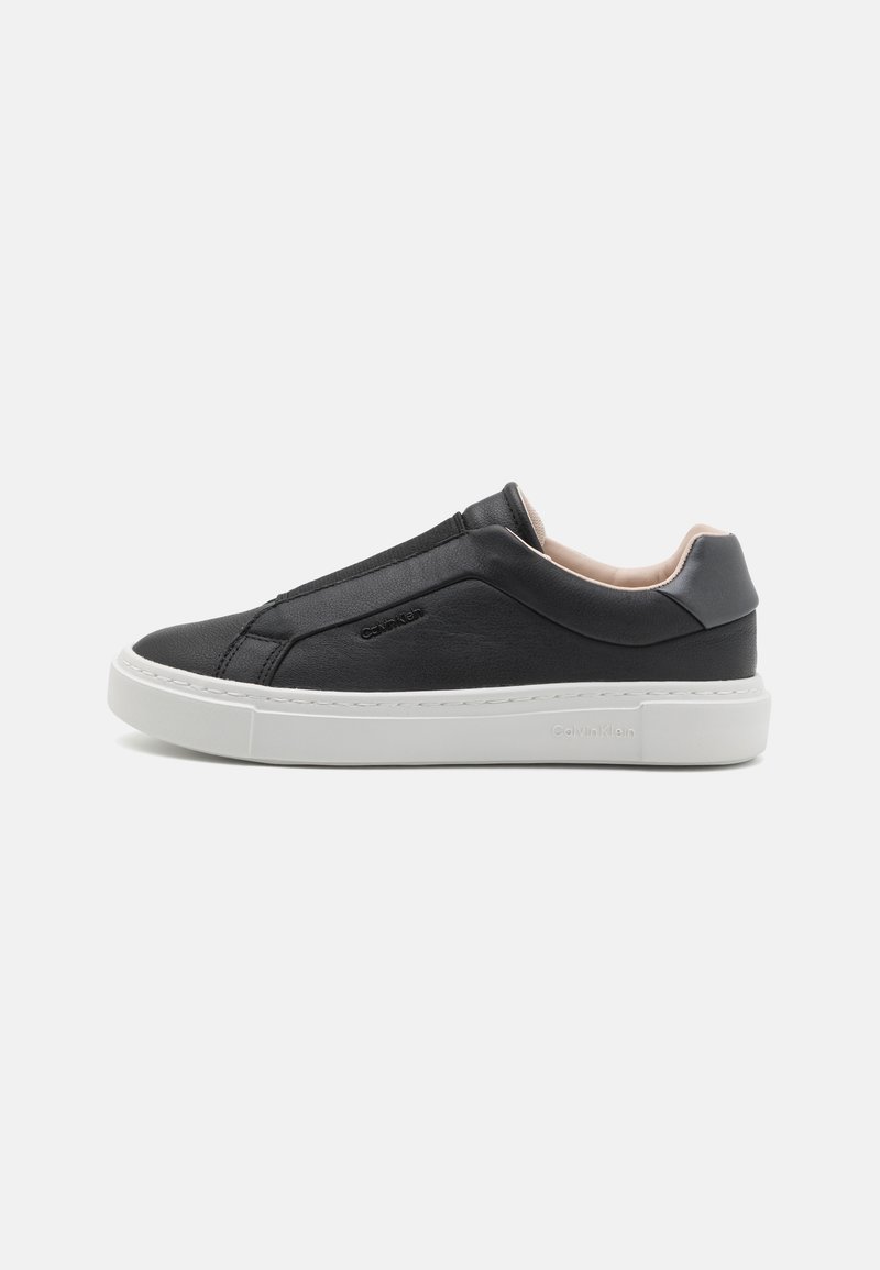 Juodos odinės slip-on sportinės kedys su baltu guminiu padu, turinčios tekstūruotą viršutinę dalį, siuvinėtus akcentus ir logotipą šone.