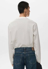 Langarmhemd in Weiß mit schwarzen horizontalen Streifen, kombiniert mit dunklen Jeans. Verfügt über einen runden Halsausschnitt und einen lockeren Schnitt.