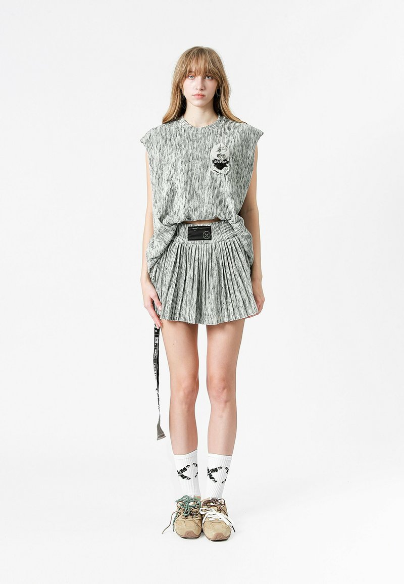 Vestido gris claro asimétrico con un patrón texturizado, que presenta un pequeño detalle de bolsillo. Combinado con una falda corta con pliegues, calcetas blancas y zapatillas.