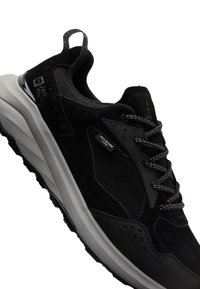 Chaussure de sport noire et grise avec panneaux en mesh et en daim, marquée "Jack Wolfskin" et "Texapore Core", avec des lacets à motifs et une semelle épaisse.