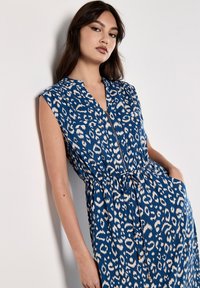 Vestito blu con pattern a leopardo, con maniche corte, chiusura con zip frontale e vita regolabile con cordoncino. Include due tasche frontali.