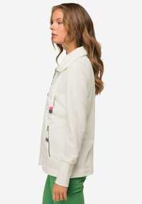 Giacca bianca con zip, colletto alto e dettagli rosa. Tessuto dal texture liscia, design aderente e tasca laterale con zip.
