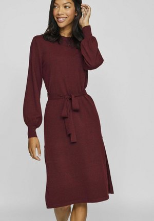 Robe en maille bordeaux avec de longues manches bouffantes, ceinture à la taille, et fente sur le côté, présentant un col rond et une texture douce.