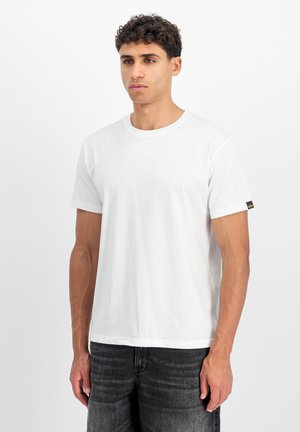 White cotton T-shirt with short sleeves, round neckline, and subtle "Alpha Industries" logo on the front. Textured black tag on sleeve.