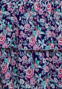 Blommig klänning i tyg med volanger, med en marinblå bakgrund och livfulla mönster i rosa, grönt och vitt.