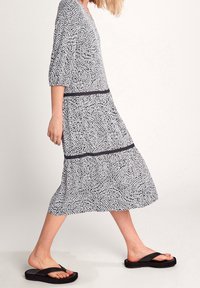 Musta-valkoinen kuviollinen midi-mekko, jossa on V-kaula-aukko, kolmannes-hihat ja tummat vaakasuorat raidat; yhdistetty mustiin flip-floppeihin.