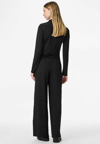 Melns top ar garām piedurknēm, kombinēts ar melnām platām biksēm ar faktūru. Apģērbs ir vienkārša dizaina bez redzamām rakstām vai rotājumiem.