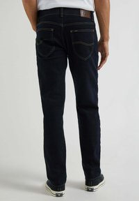 Jeans in denim blu scuro con vestibilità dritta, caratterizzati da cuciture gialle, due tasche posteriori e un'etichetta in pelle marrone nella zona della vita.