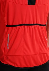 Top atlético rojo hecho de una tela elástica. Presenta detalles en negro, un escote redondo, detalles reflectantes y una cintura fruncida.