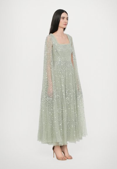 Lichtgroene paillettenjurk met een vierkante halslijn, mouwen in cape-stijl en een vloeiende rok. Bevat glinsterende details in de stof.