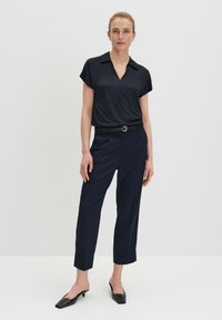 Blouse marine à col en V et manches courtes, associée à un pantalon tailleur marine. Le pantalon est doté d'une ceinture et d'une coupe cropped. Chaussures noires à enfiler.