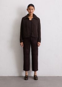 Cardigan marrone lavorato a maglia con colletto ampio e chiusura a bottoni, abbinato a pantaloni in suede marroni e mocassini scuri, design minimalista.