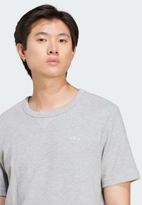 Sivý tričko s krátkym rukávom a textured vzorom s okrúhlym výstrihom. Vybavené jemne vyšitým logom Adidas na hrudi.