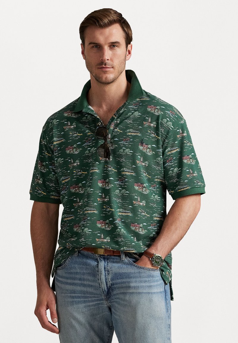 Zaļš īsu piedurkņu polo krekls, kas piedāvā laivu un māju rakstu, ar pogājamu apkakli un saulesbrillēm, kas atpūšas uz auduma.