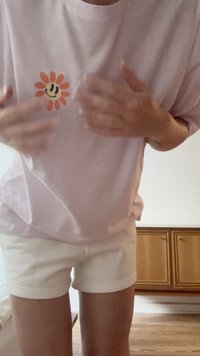 Helles rosa, übergroßes T-Shirt mit einem Blumenmotiv in Orange und Gelb auf der Brust, kombiniert mit weißen Shorts. Einfaches, lässiges Outfit.