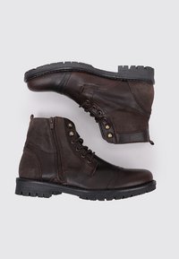 Bottes en cuir marron avec une finition texturée, lacets à l'avant, fermeture éclair sur le côté et une semelle en caoutchouc robuste avec un motif de crampons.