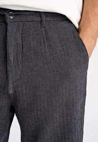 Mørkegrå bukser med fiskebensmønster lavet af struktureret stof, med knaplukning og sidelommer.