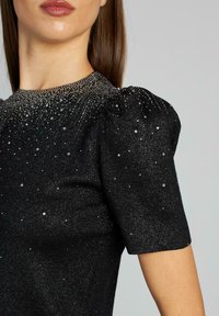 Czarna dzianinowa bluzka z krótkimi bufkami, ozdobiona srebrnymi zdobieniami i błyszczącym kołnierzykiem, z fakturowanym, błyszczącym wykończeniem.