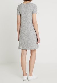 Robe grise à manches courtes en texture chinée, arrivant aux genoux, avec un décolleté rond. Portée avec des baskets blanches.