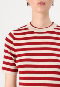 T-shirt a righe rosso e beige in maglia con scollatura rotonda e maniche corte, caratterizzato da una texture a coste e bande di colore a contrasto.